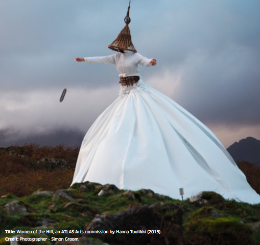 a woman in a flowing white dress and cone shaped hat walks across a dark and stormy moorland landscape