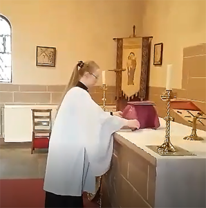 Leeanne Clark stands in her robes in front of the altar and lays out items for communion