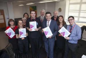 Minister for Business, Fair Work and Skills, Jamie Hepburn MSP stands front and centre holding a copy of the report, surrounded by Eddie, Kieran and Kirsty, their job coaches and SCLD staff, holding reports and smiling