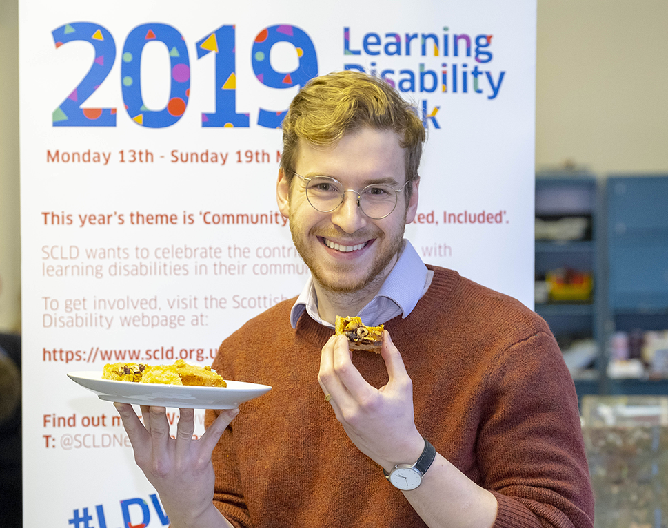 Minister for Business, Fair Work and Skills, Jamie Hepburn MSP stands front and centre holding a copy of the report, surrounded by Eddie, Kieran and Kirsty, their job coaches and SCLD staff, holding reports and smiling