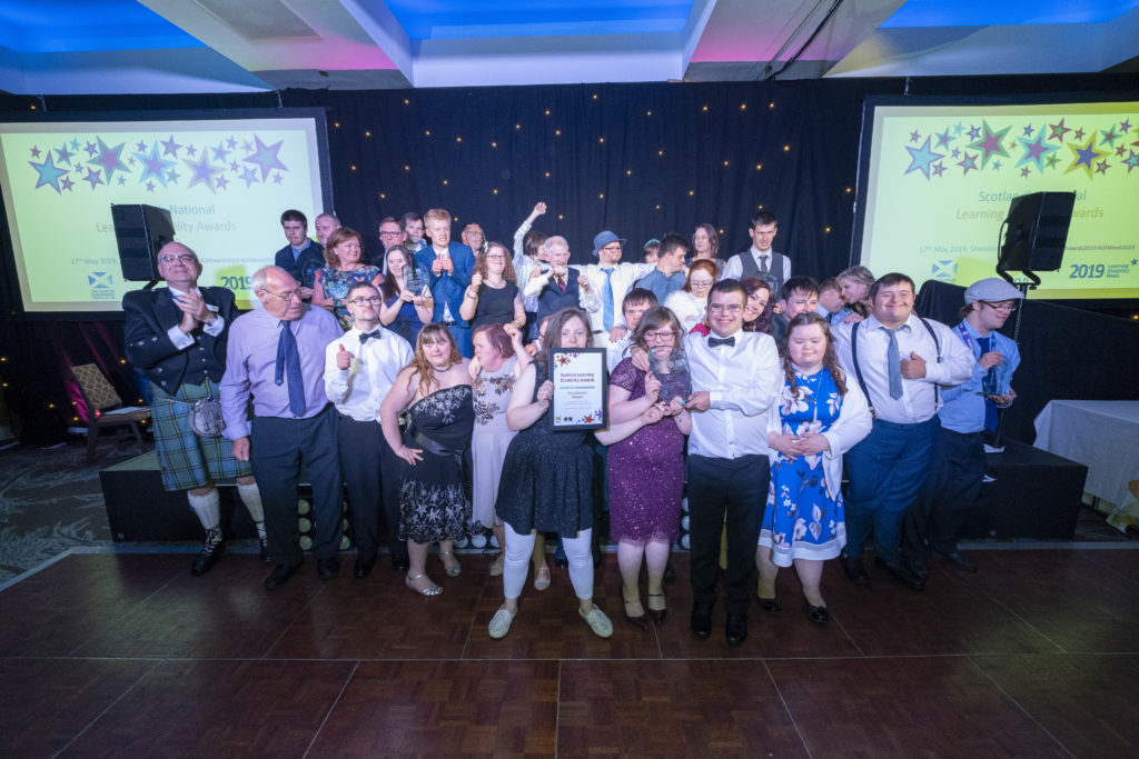 All the 2019 finalists smile and cheer whilst holding their awards on stage at the Learning Disability Awards 2019