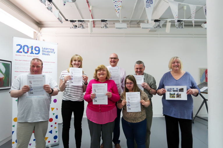 people stand smiling with copies of the 'How's Life?' survey at the survey launch event