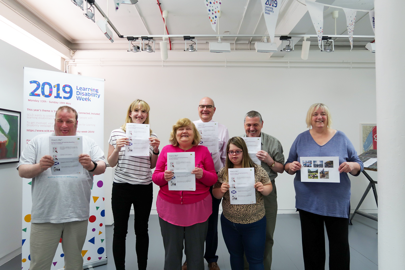 James Morton, celebrity baker stands in front of a Learning Disability Week banner smiling and eating cake