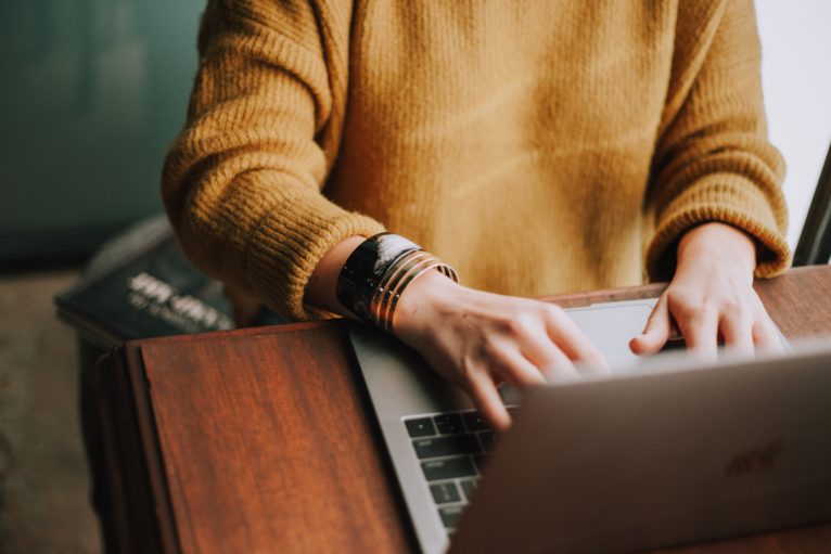 A person sits typing on their laptop at home.