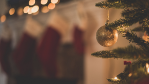 A Christmas tree with bauble. Stockings hang on a fire place in soft focus.